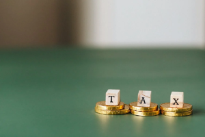 An image of the letters “TAX” stacked on top of gold coins 