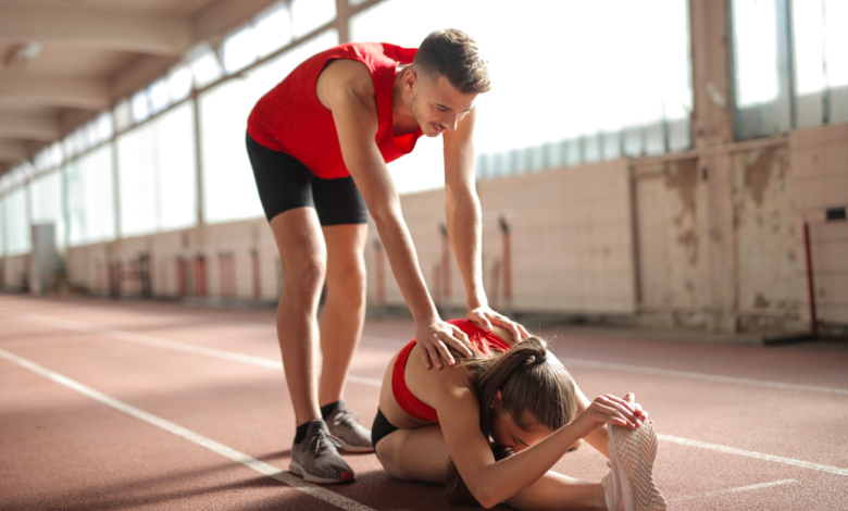 A trainer helps his client stretch by placing his hands on her back.