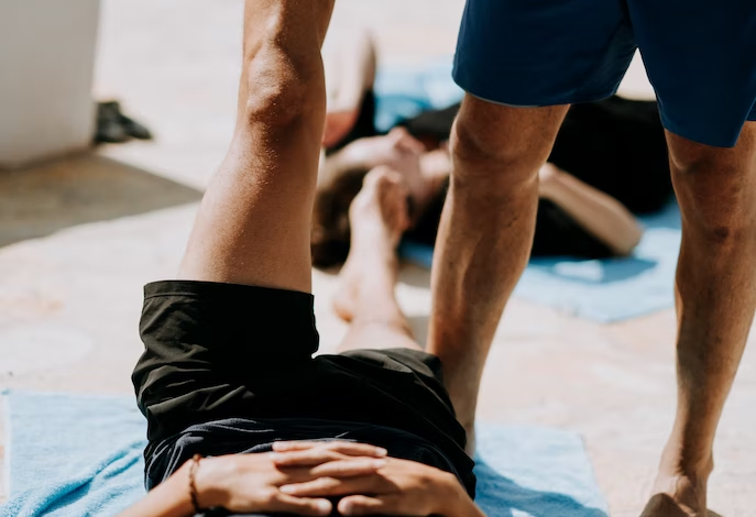A trainer helps his client perform a deeper stretch during a yoga workout.